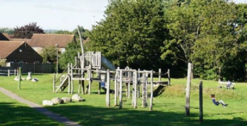 Picture of a children's park on a field, in the background there are some residential buildings. 